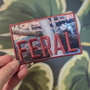 May include: Red embroidered patch with the word "FERAL" in white lettering. The patch features a photo of a possum in a wooded area.