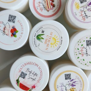 May include: An assortment of white, 2 oz sample jars of body butter with various scents. Labels include "Pearberry", "Strawberry Shortcake", "Watermelon Sunshine", "Warm Sugar Vanilla", and "Just Peachy". Each jar has a QR code.