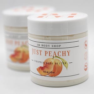 Puede incluir: Un tarro blanco con un diseño de melocotón y el texto "IM BODY SHOP JUST PEACHY - WHIPPED BODY BUTTER - 113.4g 4 fl oz"