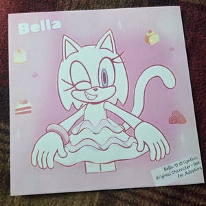 May include: A square print featuring a pink-toned illustration of a cat character named Bella. The character winks and wears a ruffled dress. Small dessert icons surround the figure. The text Bella and a copyright notice are visible.