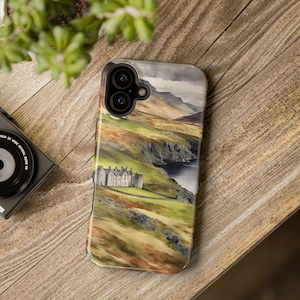 Może przedstawiać: Etui na telefon z akwarelowym wzorem kamiennego budynku na klifie z widokiem na zbiornik wodny. Etui ma wycięcie na aparat z dwoma obiektywami.