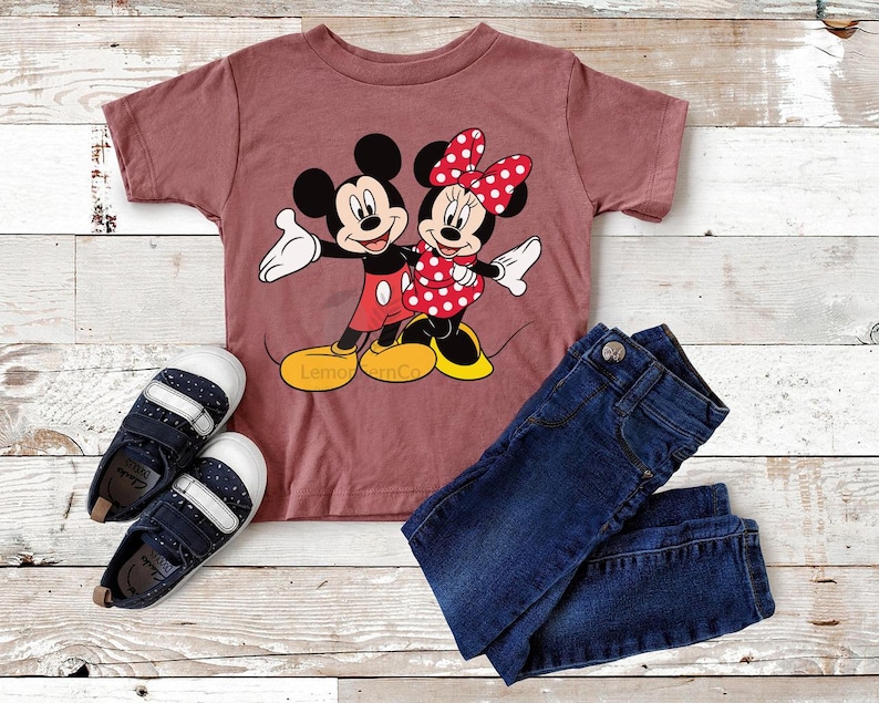Może przedstawiać: Str&oacute;j dziecięcy składający się z bordowej koszulki z grafiką Myszki Miki i Myszki Minnie, ciemnoniebieskich dżins&oacute;w oraz granatowo-białych tenis&oacute;wek. Koszulka ma u dołu napis "Lemon & Co".