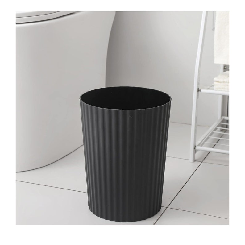 May include: A black, cylindrical waste bin with a ribbed texture. The bin is made of plastic and has a smooth, rounded top.