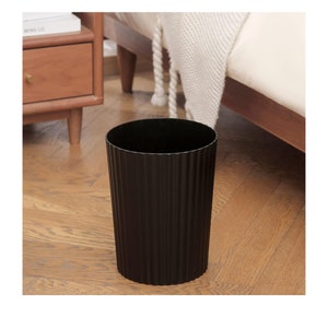 May include: A black, cylindrical waste bin with a ribbed texture. The bin is sitting on a wooden floor.