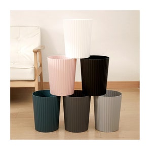 May include: Six plastic waste bins in different colours, stacked in a pyramid shape. The bins have a ribbed texture and are in the colours white, pink, black, dark grey, and light grey.