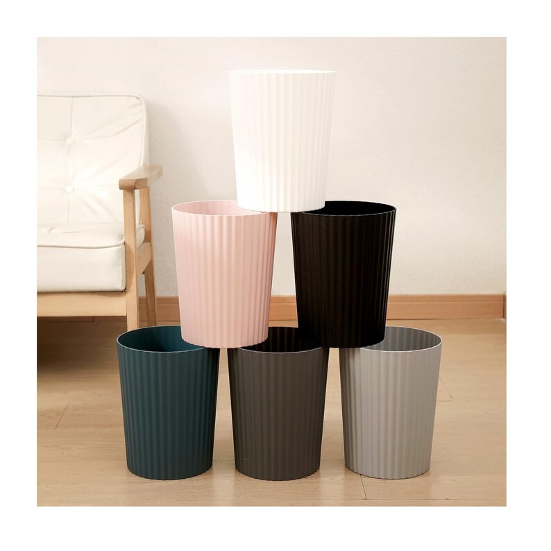 May include: Six plastic waste bins in different colours, stacked in a pyramid shape. The bins have a ribbed texture and are in the colours white, pink, black, dark grey, and light grey.