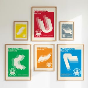 May include: A collection of framed posters featuring Washington D.C. Metro lines. Each poster has a solid color background with a stylized line graphic and the line's name. The Red, Green, Orange, and Blue lines are displayed.