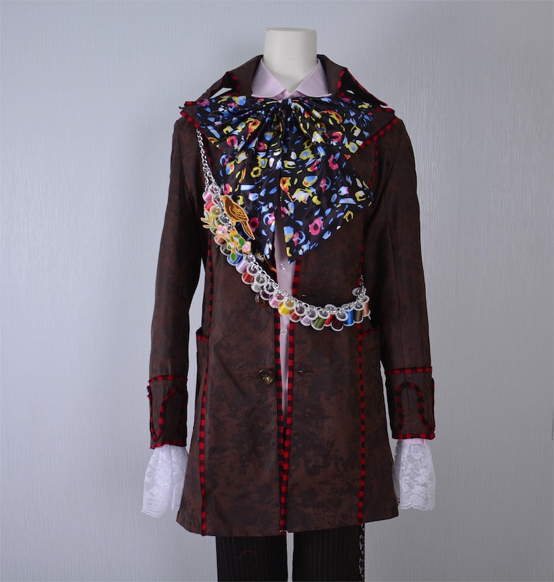 May include: A brown long-sleeved coat with red trim and a white lace collar. The coat has a colorful patterned bow tie and a chain with colorful beads.