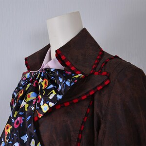 May include: A brown jacket with a red and black checkered trim. The jacket has a large, ruffled collar with a colorful floral pattern.