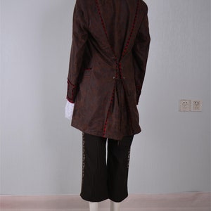May include: A brown jacket with red trim and a lace-up back. The jacket is worn over black pants with a white shirt underneath.