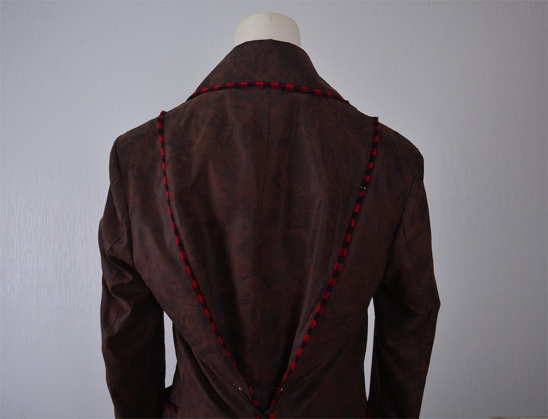 May include: Brown suede jacket with red and black trim. The jacket has a collar and long sleeves.