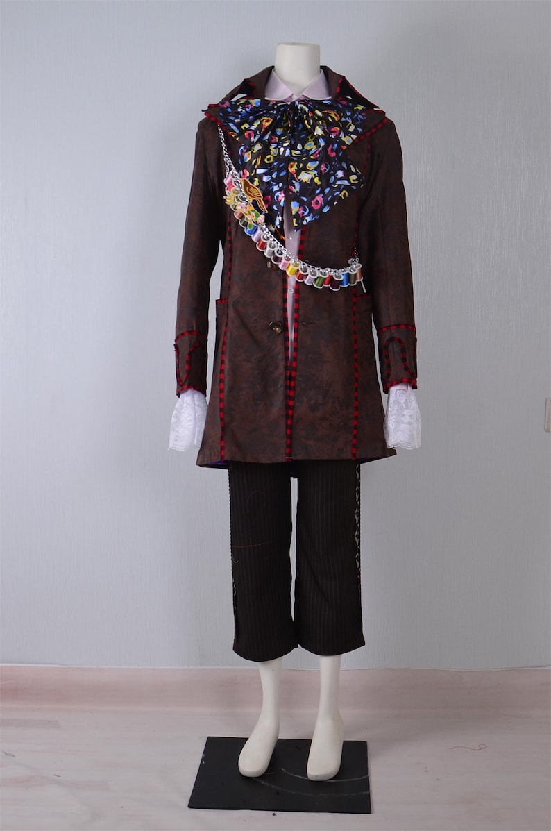May include: A brown coat with red and white trim, a white shirt with a pink bow tie, a black and white patterned scarf, and a chain with colorful charms. The coat has a pocket on the left side. The pants are black with white stripes.