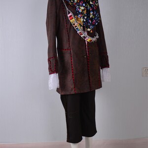 May include: A brown long-sleeved jacket with red stitching, a white lace trim, and a colorful patterned scarf. The jacket has a chain with colorful beads and a button closure.