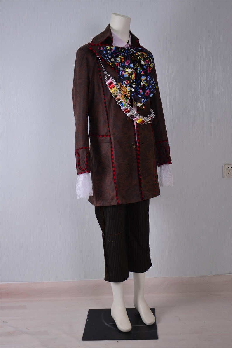 May include: A brown long-sleeved jacket with red stitching, a white lace trim, and a colorful patterned scarf. The jacket has a chain with colorful beads and a button closure.
