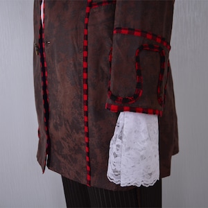May include: A brown jacket with red and black plaid trim. The jacket has a single button closure and a white lace trim on the sleeve.