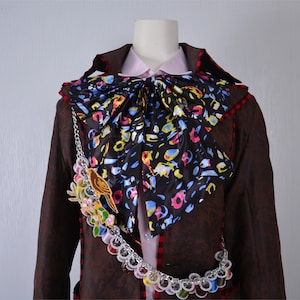 May include: A brown jacket with a colorful patterned bow tie and a chain with colorful beads and a bird charm.