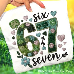 Könnte beinhalten: Weißes T-Shirt mit gesticktem Design. Das Design enthält die Wörter "six seven" und die Zahlen "67" in schwarzer Schrift. Die Zahlen und Wörter sind mit grünen, rosa und blauen Blumen- und Herzmotiven verziert. "PNG Digital Download Only" ist unten aufgedruckt.