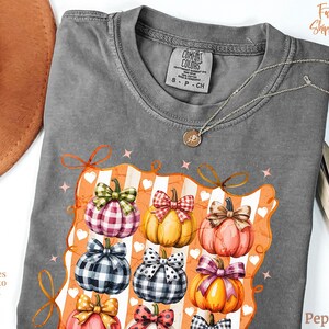 May include: Gray Comfort Colors t-shirt with a colorful pumpkin graphic. The graphic features pumpkins with various plaid and polka dot bows. The shirt has the text "Sizes up to 4X" on the left side.
