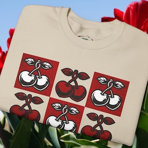 May include: A beige t-shirt with a red and white cherry design. The cherries are arranged in a checkered pattern.