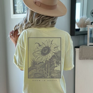 May include: A light yellow t-shirt with a black and white sunflower graphic and the text "GROW IN GRACE" printed on the back.