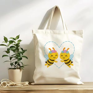 Peut inclure: Un sac fourre-tout cr&egrave;me avec un motif de dessin anim&eacute; de deux abeilles souriantes &agrave; l'int&eacute;rieur d'un contour de c&oelig;ur bleu. Les abeilles sont jaunes et noires avec des couronnes de fleurs et des ailes bleues. Le sac a une poign&eacute;e simple.
