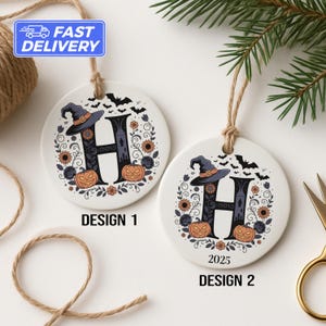 May include: Two white ceramic Halloween ornaments with the letter "H" in a black witch hat design. The ornaments feature pumpkins, bats, and floral accents. One ornament says "Design 1" and the other says "2025 Design 2".