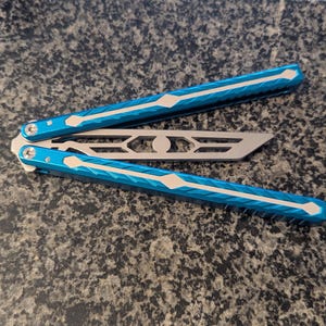 May include: A blue and silver butterfly knife with a patterned handle. The knife is open and the blade is visible.