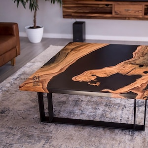 Puede incluir: Mesa de centro cuadrada con tapa de resina epoxi negra y patrones de vetas de madera natural. La mesa tiene una estructura de metal negro. El logotipo "Craft House" es visible.
