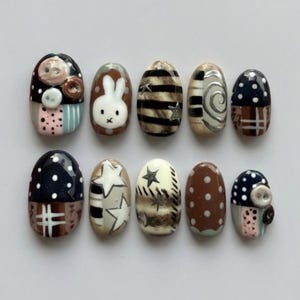 May include: A collection of ten artificial nails with diverse designs. The nails showcase patterns such as polka dots, stripes, stars, and a bunny face. Colours include brown, white, black, and pink, with some nails decorated with small buttons.