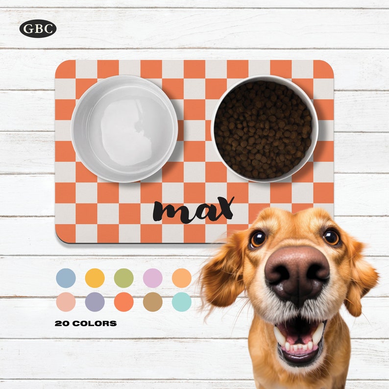 May include: A checkered orange and white pet food mat with two white bowls. One bowl is filled with brown dog food and the other is empty. The mat has the name "max" written on it in black.