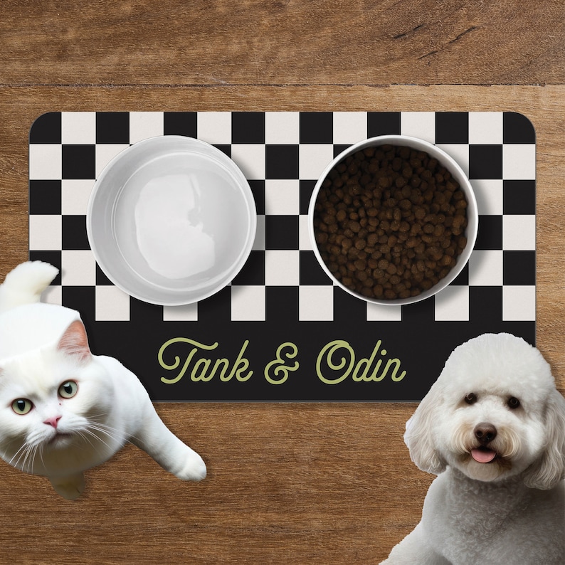 May include: A black and white checkered pet feeding mat with two white ceramic bowls. One bowl is filled with dry dog food and the other is empty. The mat has the text "Tank & Odin" in green lettering.