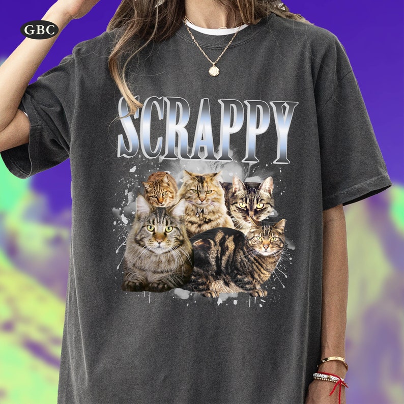 May include: A gray t-shirt with the word "SCRAPPY" printed in white and a graphic of several cats. The cats are in various poses and have different fur patterns.