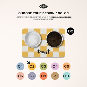May include: A yellow and white checkered pet food mat with two white bowls. One bowl is empty and the other bowl is filled with brown pet food. The mat has the word "toast" written on it in black. There are ten color swatches below the mat.