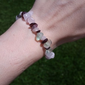 Op de afbeelding: Een armband gemaakt van roze, groene en paarse edelsteen kralen. De armband zit om een pols.