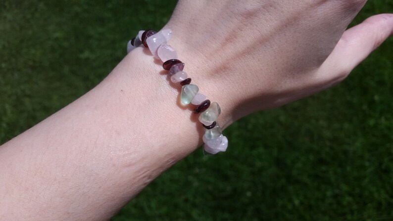 Op de afbeelding: Een armband gemaakt van roze, groene en paarse edelsteen kralen. De armband zit om een pols.