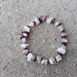 Op de afbeelding: Een armband gemaakt van verschillende halfedelstenen, waaronder roze, groene, paarse en rode stenen. De armband is gemaakt van kleine, onregelmatig gevormde stenen.