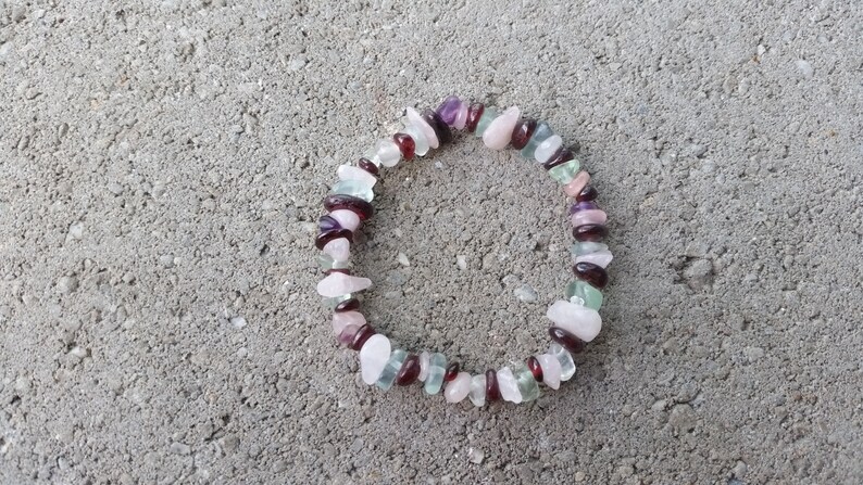 Op de afbeelding: Een armband gemaakt van verschillende halfedelstenen, waaronder roze, groene, paarse en rode stenen. De armband is gemaakt van kleine, onregelmatig gevormde stenen.
