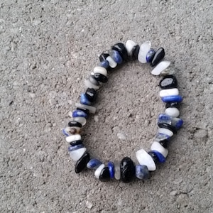 May include: A bracelet made of black, white, and blue gemstone beads. The beads are irregularly shaped and strung together on a clear elastic cord.
