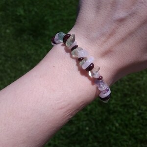 Op de afbeelding: Een armband gemaakt van groene, paarse en roze stenen. De armband zit om een pols.