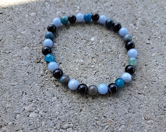 May include: A beaded bracelet with blue, black, and gray stones. The bracelet is made of natural stones and is designed to be worn on the wrist.