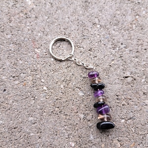 May include: A silver key chain with a charm made of amethyst, smoky quartz, and black onyx beads.