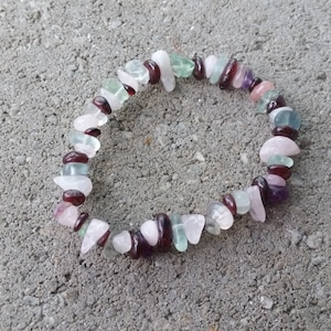 Op de afbeelding: Een veelkleurige edelsteen armband met roze, groene en rode stenen. De armband is gemaakt van kleine, onregelmatig gevormde stenen.