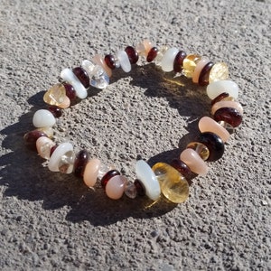 May include: A bracelet made of various semi-precious stones, including white, peach, yellow, and brown stones.