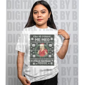 May include: White t-shirt with a graphic design featuring text and an image. The text includes "ESA NO PORQUE ME MEO" and "FELIZ NAVIDAD PERROS!". The design also includes a picture of a person and snowflake patterns.
