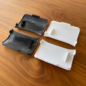 Op de afbeelding: Vier kunststof autodeurgreepbedekkingen, twee zwart en twee wit. De bedekkingen zijn ontworpen om over de bestaande deurgreep te passen.