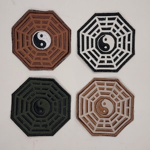 May include: Four octagonal patches with a yin yang symbol in the center. The patches are brown, black, green, and beige. Each patch has a circular design with eight spokes radiating from the center.