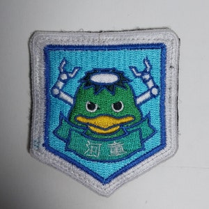 May include: A blue and green embroidered patch featuring a cartoon duck with a halo, wearing a green shirt and holding a banner with the text "River" in Japanese characters.