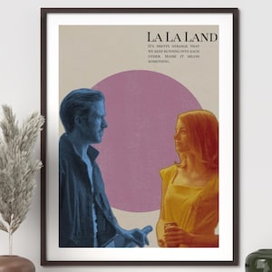 Puede incluir: Un póster enmarcado de la película "La La Land". La imagen muestra dos figuras en tonos azules y amarillos, sobre un círculo rosa. El título de la película y una cita están impresos en la parte superior.