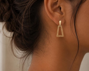 May include: A gold-toned drop earring featuring a solid triangular top piece connected to an open, trapezoidal frame with a detailed, intricate lattice or mesh pattern throughout the lower section, suspended from a secure post-back closure.
