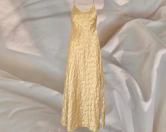 Könnte beinhalten: Langes, hellgelbes Slipkleid mit Spaghettiträgern. Das Kleid hat ein strukturiertes, zerknittertes Aussehen und einen leichten Glanz. Der Stoff fällt bis zum Boden, und das Kleid hat einen dezenten Schlitz an der Seite.
